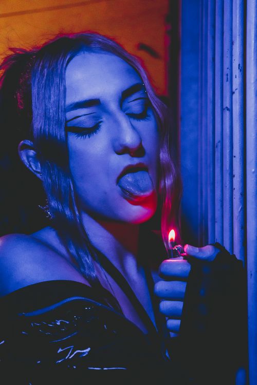 Free Vibrant portrait of a woman with neon blue and red lighting holding a lighter. Stock Photo
