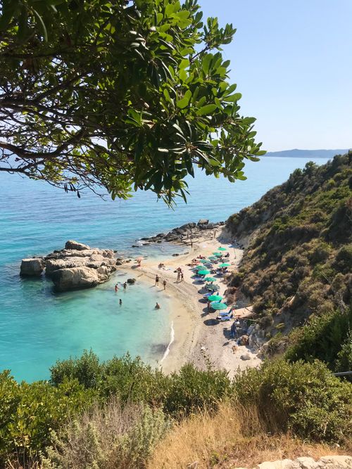 Free Aerial view of a serene beach cove with turquoise waters and sunbathers under umbrellas. Stock Photo