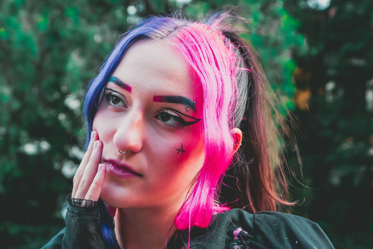young woman with vibrant colored hair and artistic makeup posing outdo