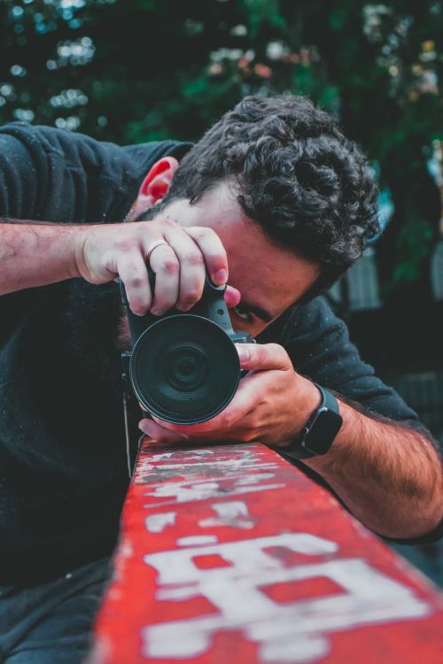 Free Photographer focusing through DSLR camera, capturing a dynamic shot outdoors. Stock Photo