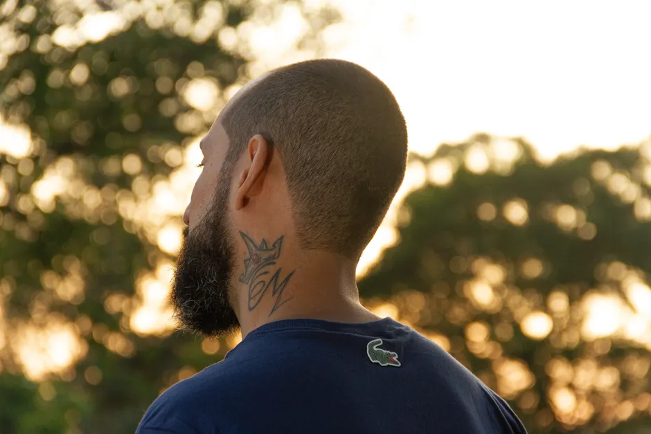 Homme de dos au coucher du soleil, couronne et initiales tatouées sur le côté du cou