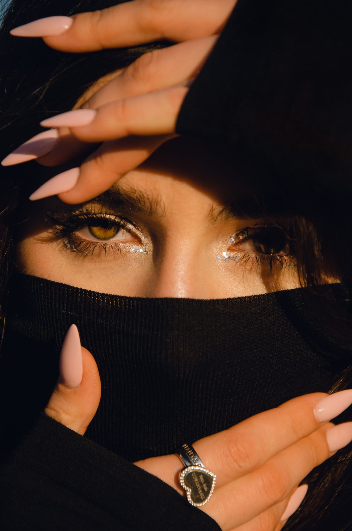 Close-up of a woman with glitter eyeshadow and pink nails, partially obscured by fabric. Fashionable and stylish portrait.