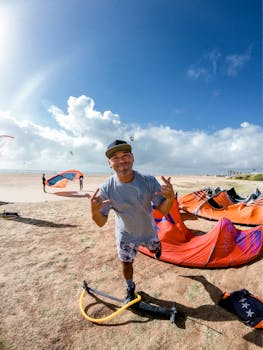 Man enjoying kite surfing on a sunny beach with colorful kites and a bright sky.