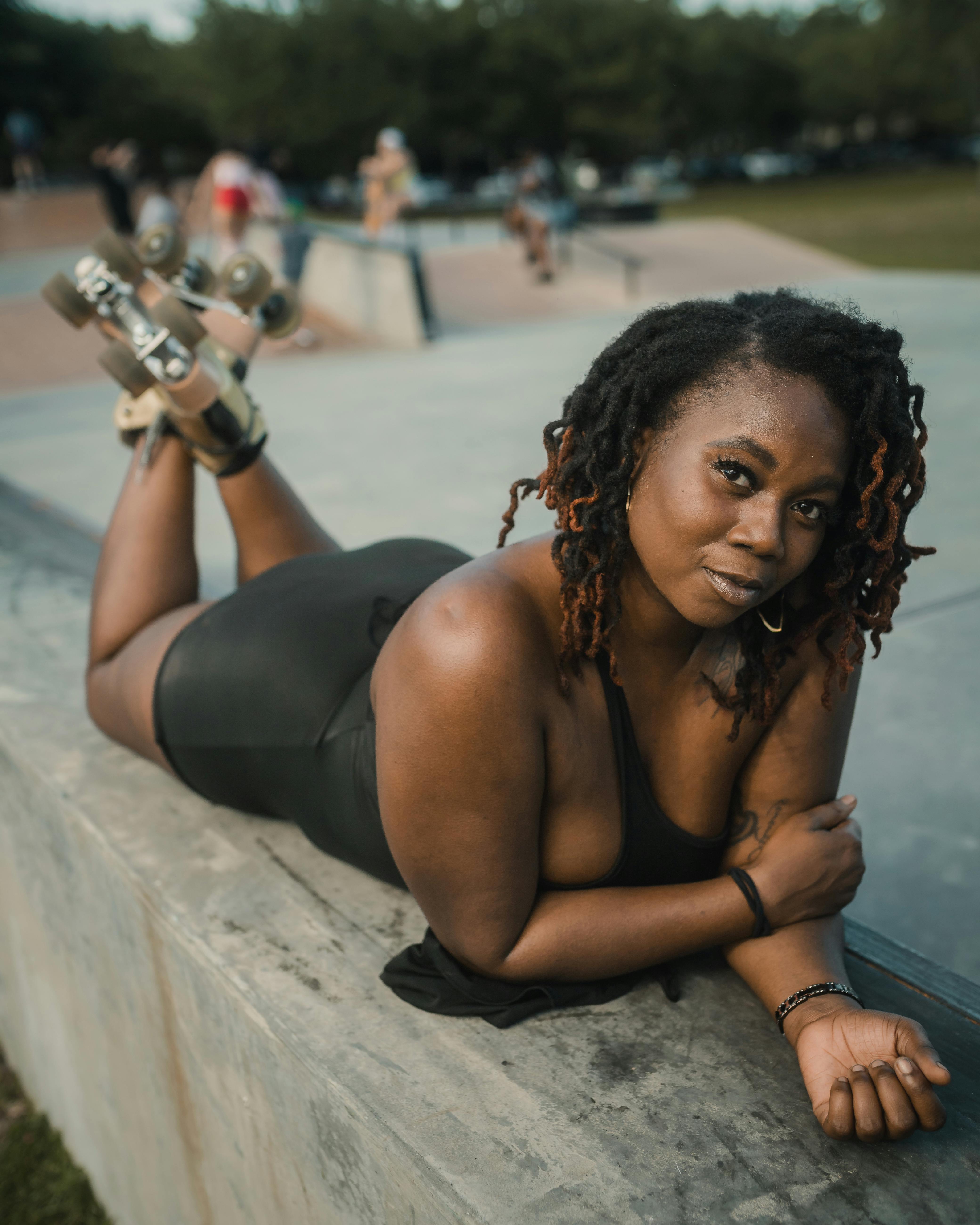 Adult woman lying down at skatepark, posing with vintage rollerskates on concrete edge.
