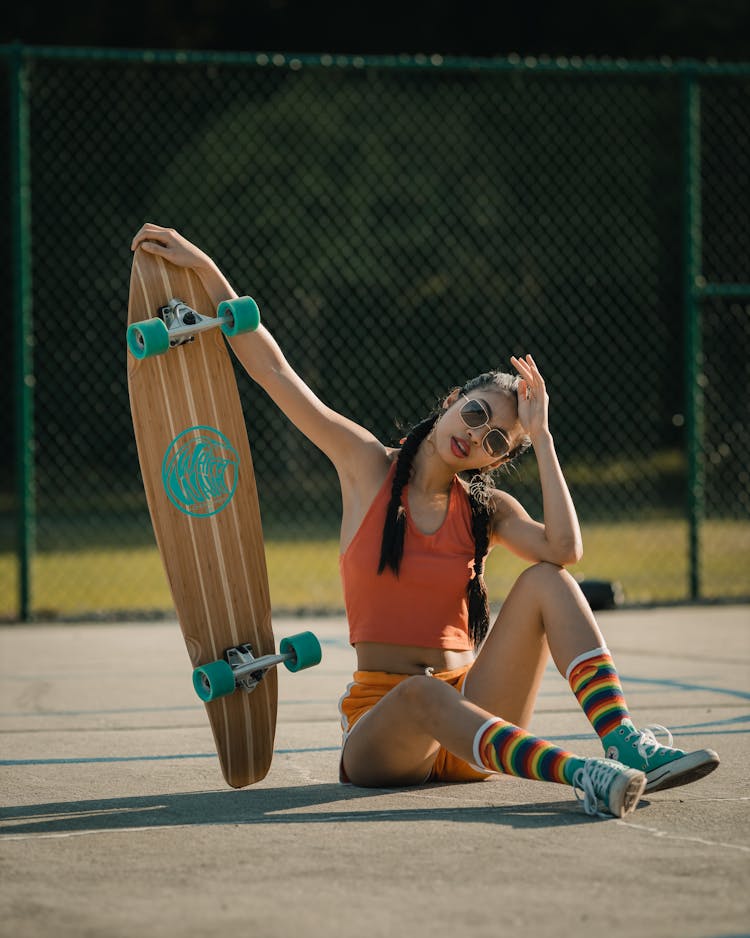 Woman Sitting On Ground Holding A Longboard