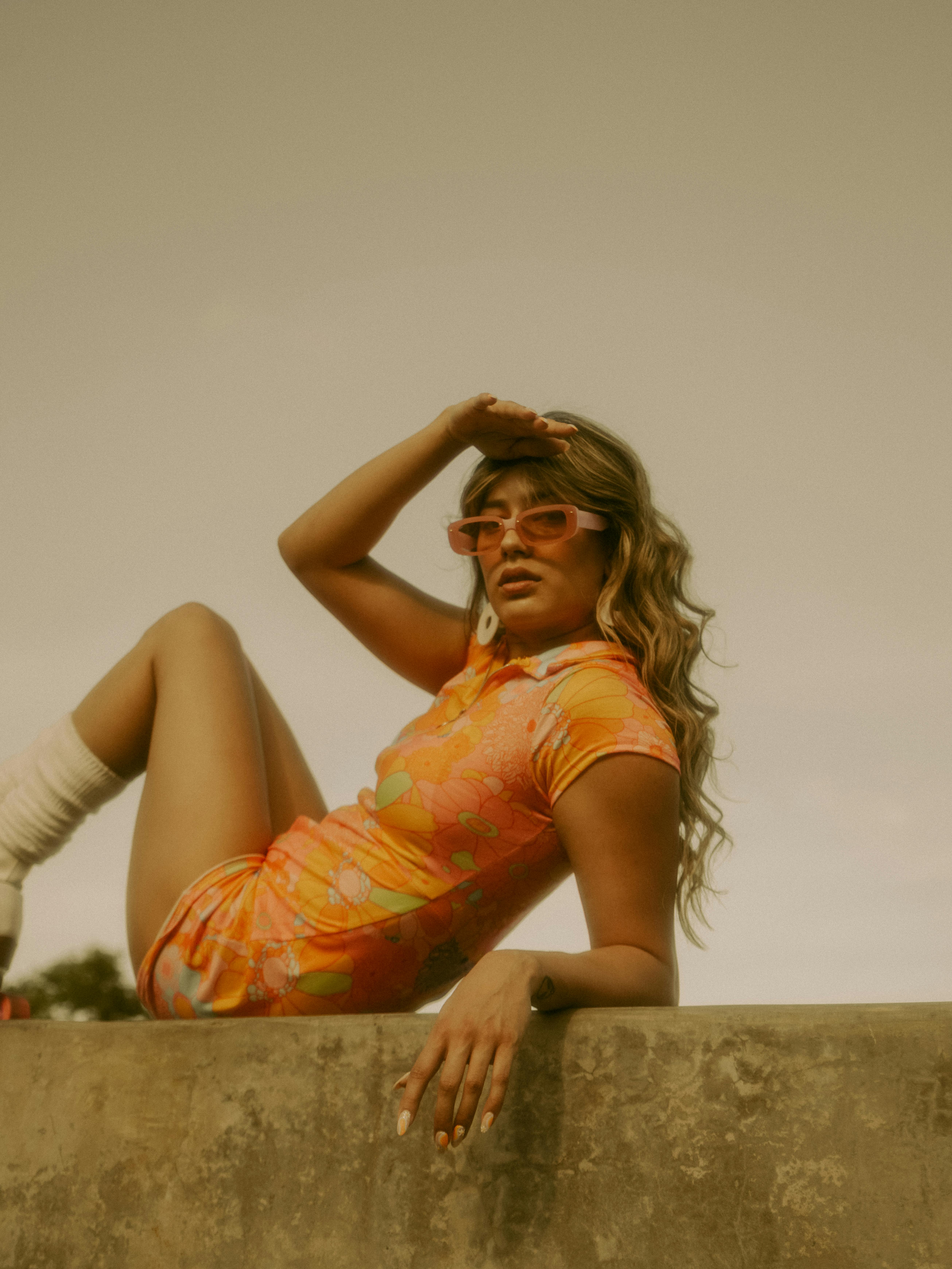 Stylish woman in orange mini dress with sunglasses basking in outdoor sunlight.