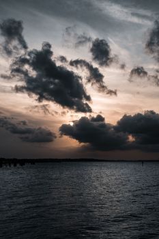 A scenic view of dramatic clouds over a calm sea during sunset, creating a moody atmosphere.