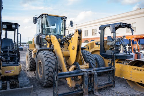 Yellow and Black Heavy Equipment Parked Beside a Compactor