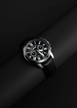 Sophisticated silver watch with black leather strap against a dark background.
