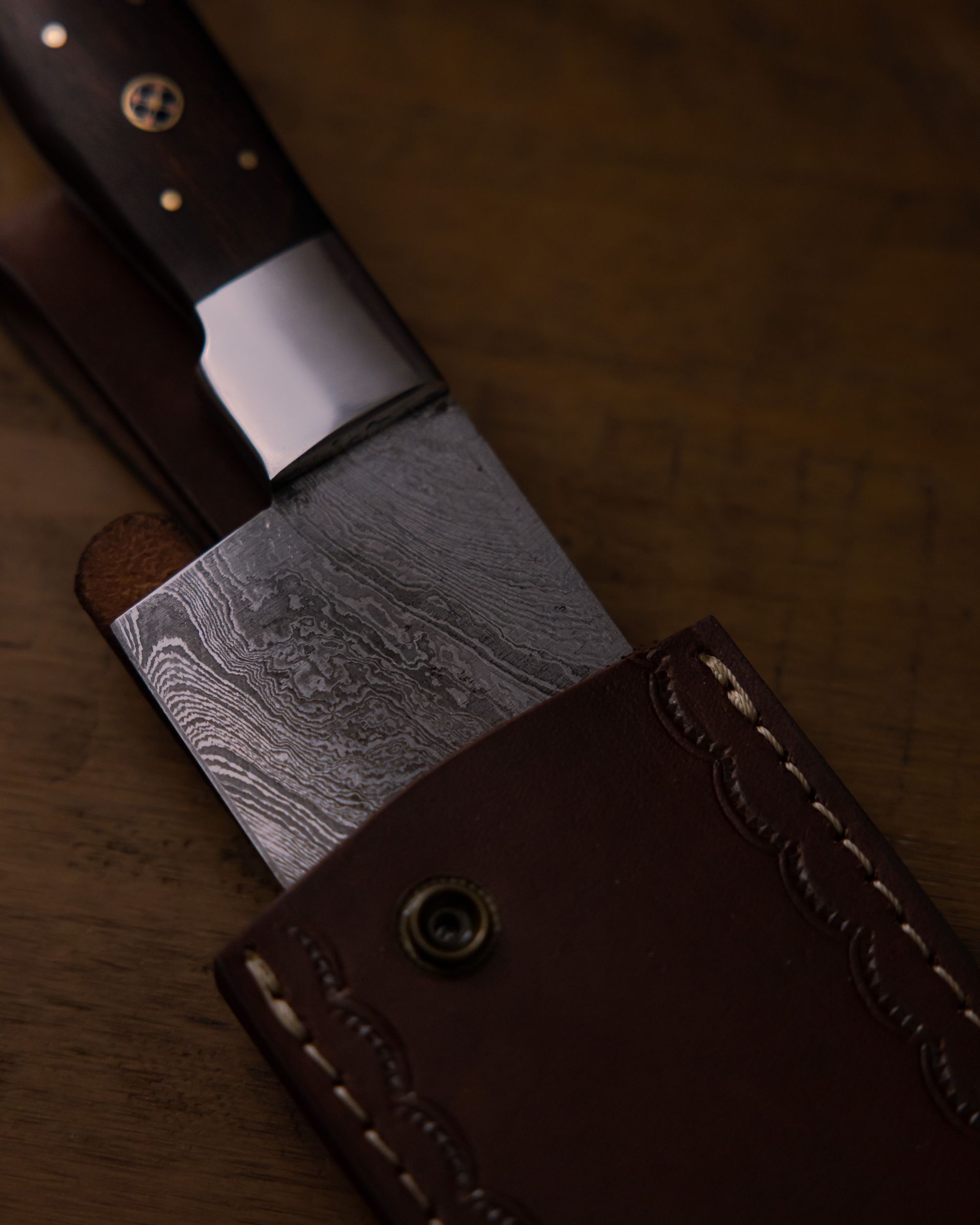 Detailed image of a Damascus steel knife partially encased in a crafted leather sheath