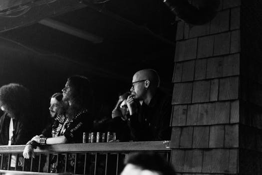 Black and white image of a group of adults attentively watching a concert indoors.