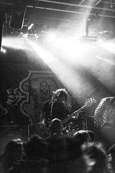 Monochrome photo of a dynamic live music performance with guitarists and crowd interaction.