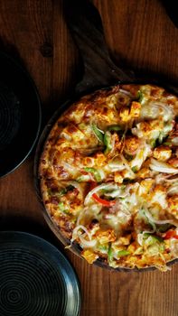 Savor the flavors of a cheese-loaded paneer pizza with vegetables, served on a rustic wooden tray.