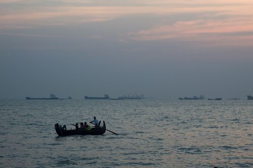 Free Tranquil scene of people rowing a boat at twilight, surrounded by the vast ocean and distant ships. Stock Photo