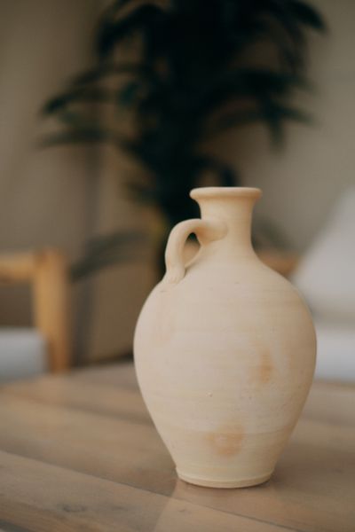 Stoneware jug on a wooden table with a plant behind it — photo by ZUMRAD NORMATOVA on Pexels