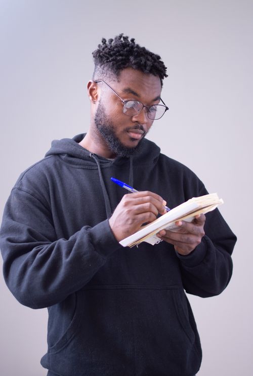 Free A focused man in a hoodie writing in a notebook, displaying concentration and casual style. Stock Photo