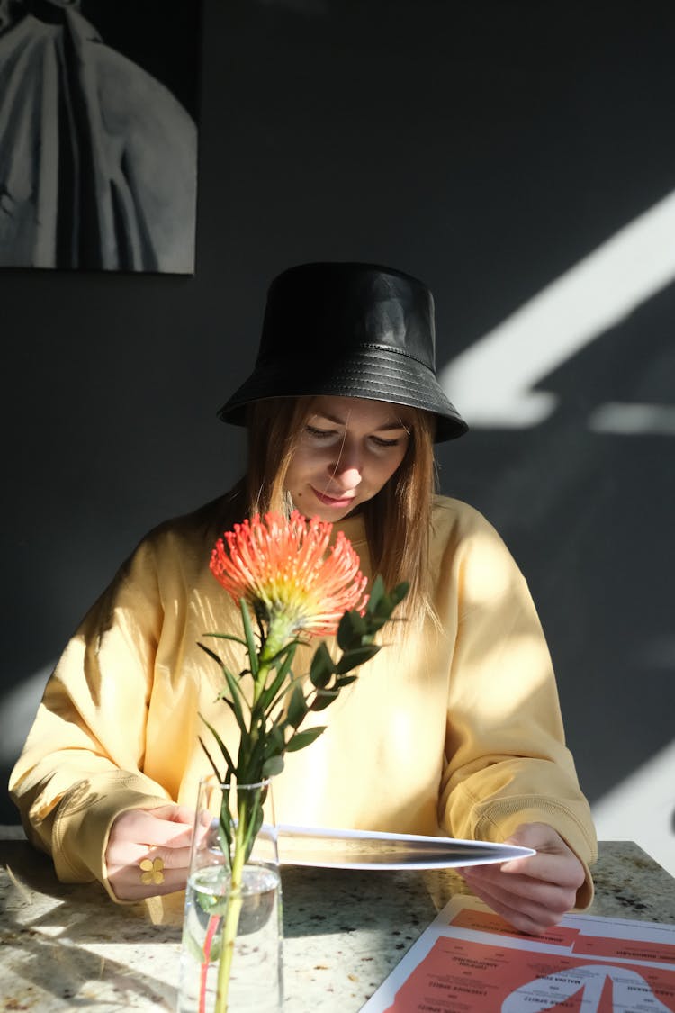 A Woman In A Bucket Hat And A Yellow Sweater Reading A Menu