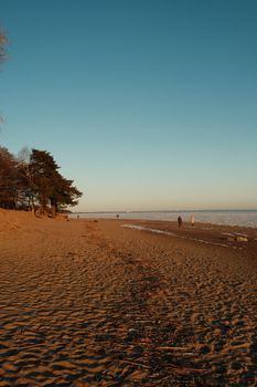 Golden sand and tranquil sea under a vibrant sunset sky with distant beach walkers.