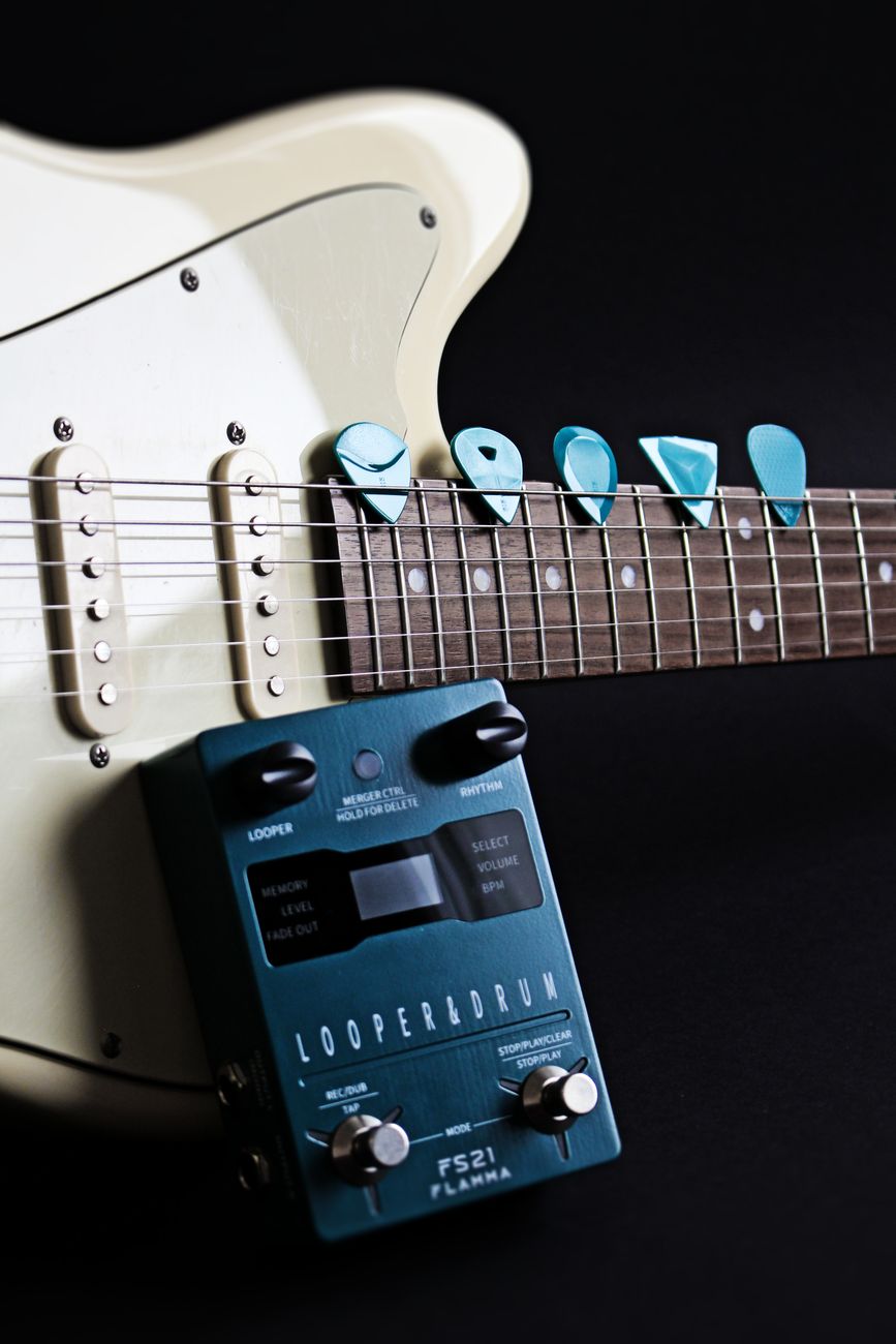 Close-up of an electric guitar with picks and a looper pedal on a dark background.