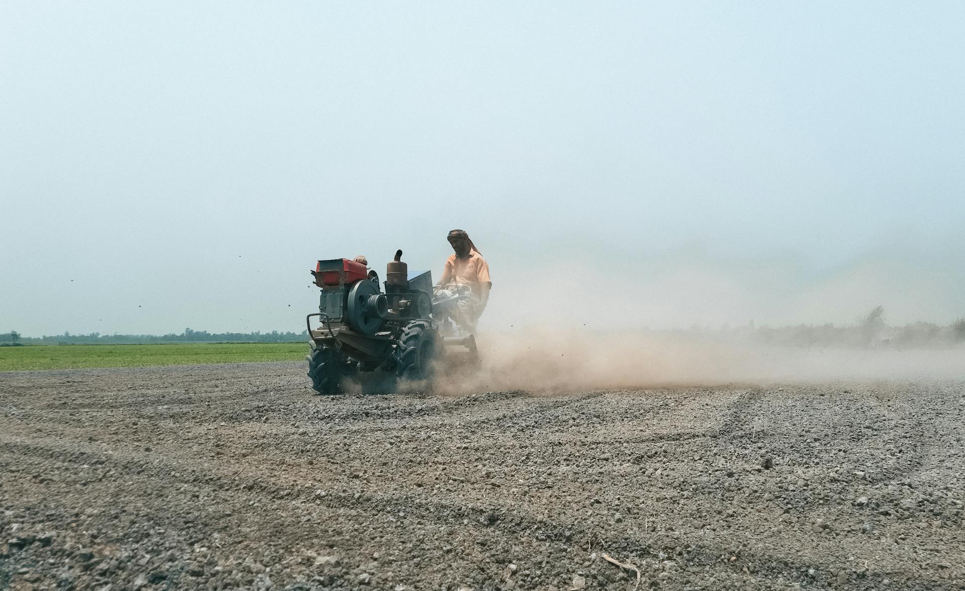 A farmer operates a tractor to plow a dusty field in Pabna, Bangladesh, capturing rural agricultural life.