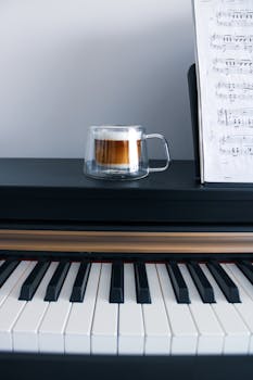 Glass coffee mug on a piano with sheet music, perfect for music-themed stock photos.