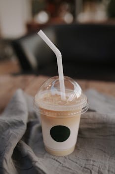 A close-up of a plastic cup with iced coffee and a straw, set on a wooden table.