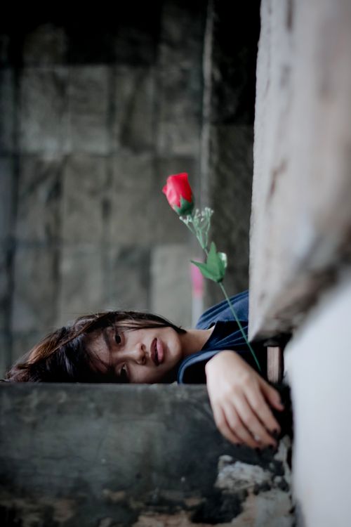 Free A reflective portrait of a young woman reclining with a red rose, conveying depth and emotion. Stock Photo