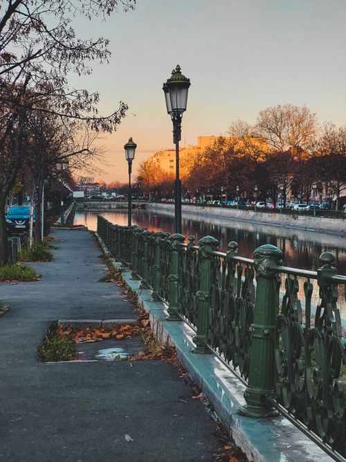 Free Picturesque view of a tranquil riverside walkway in Bucharest during sunset, surrounded by autumn foliage. Stock Photo