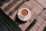 A cup of coffee on a wooden table in the sunlight creates a warm, inviting ambiance.