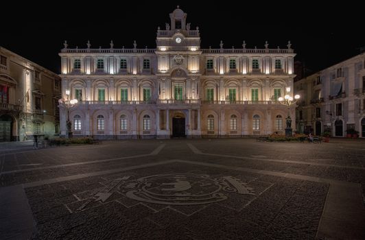 Night view of the illuminated Palazzo dell'Università in Catania, Italy, showcasing its historical facade.