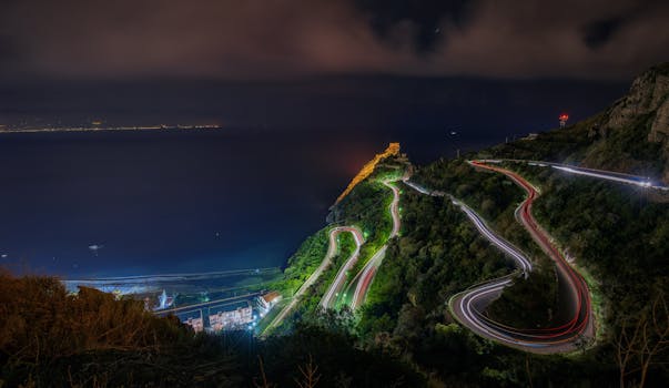 Stunning nighttime view of Forza d'Agrò, Sicilia with winding roads and ocean in view.