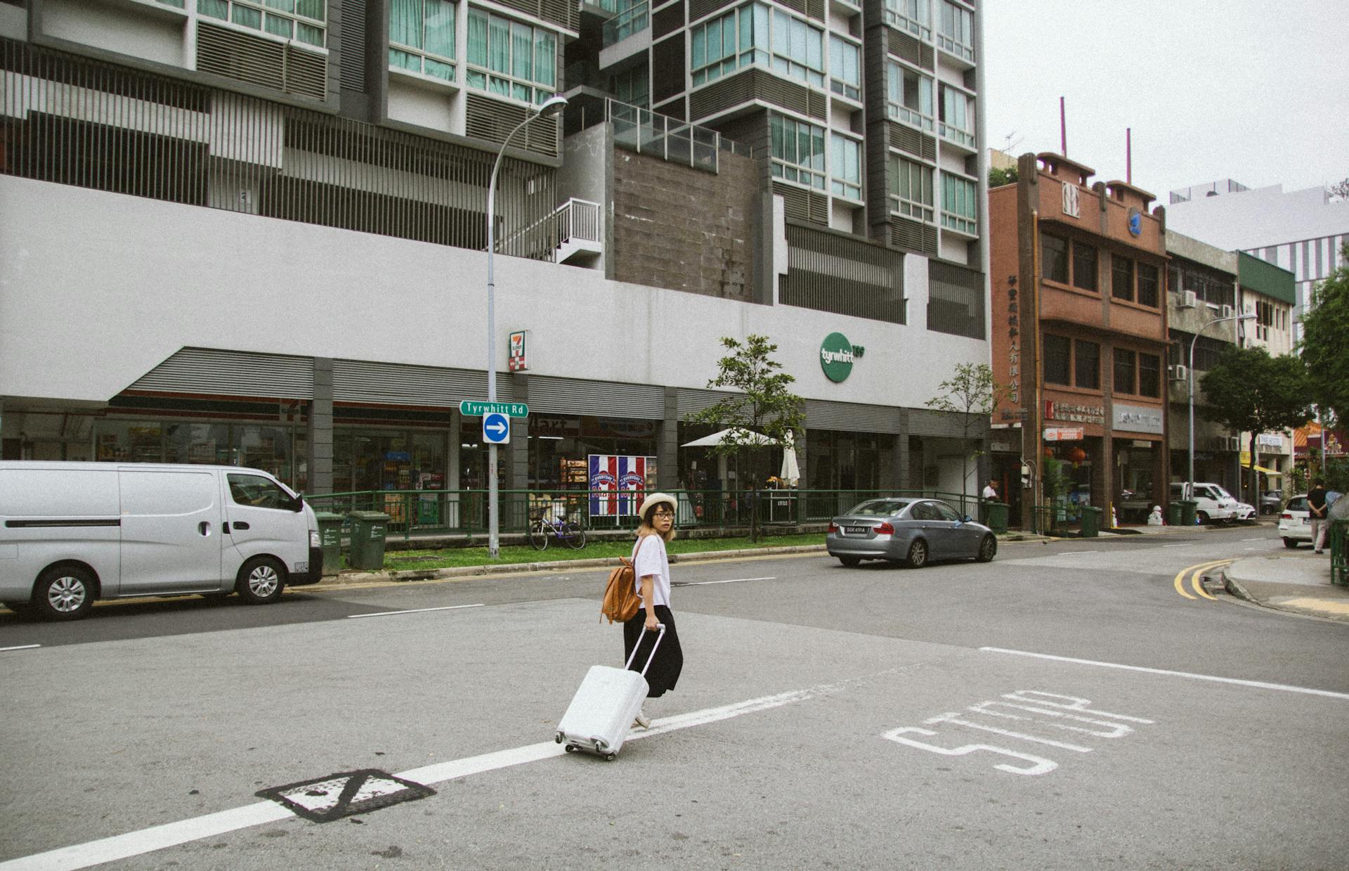 Woman with suitcase crossing a city street surrounded by urban architecture in daylight.