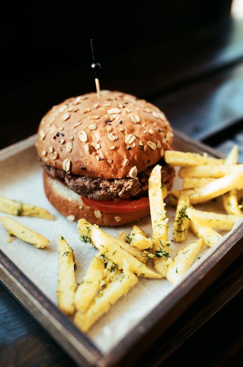 Free Mouthwatering burger with sesame bun and seasoned fries on a wooden tray. Stock Photo