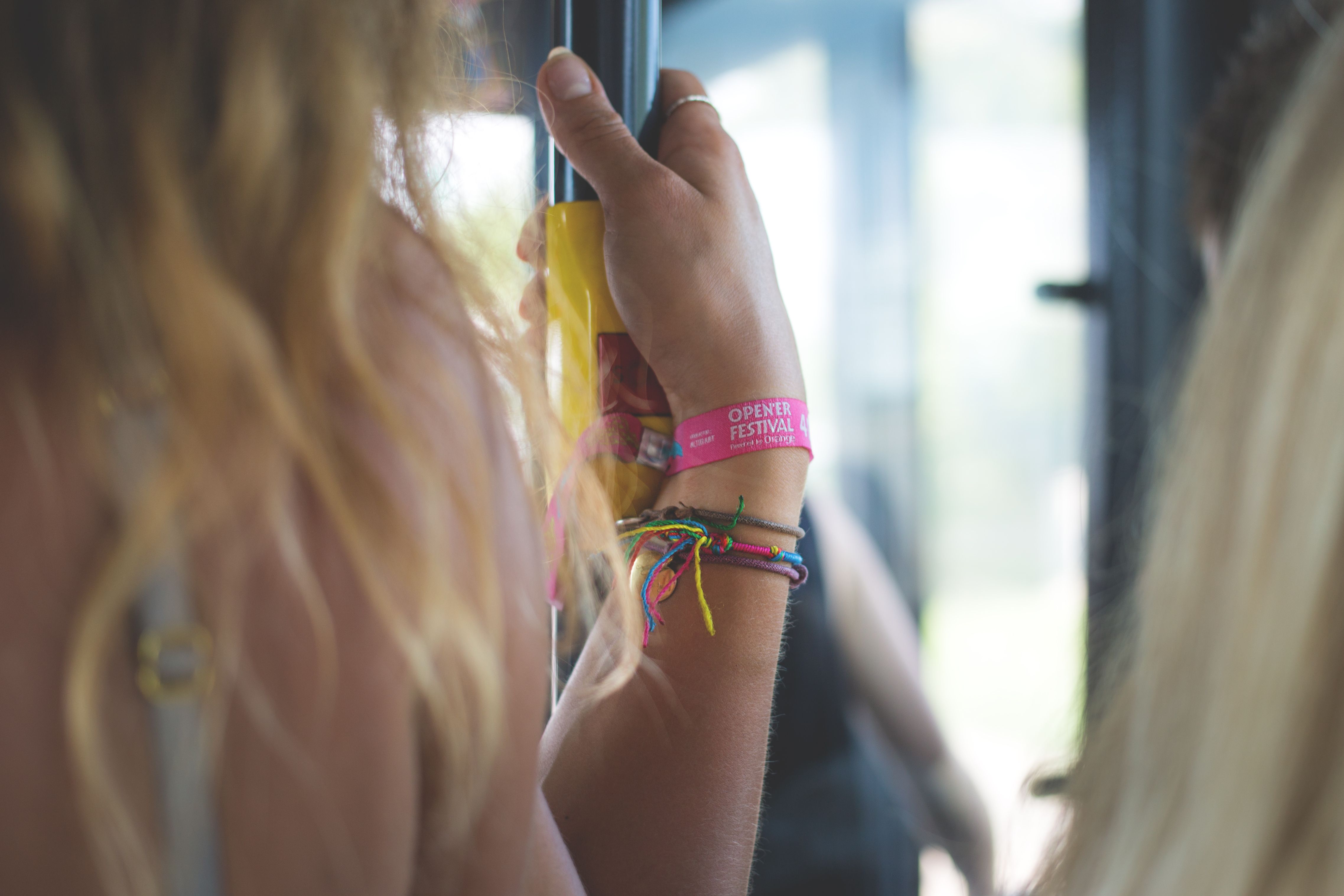 Close-up of a woman with festival wristbands holding a bus handle in summer.