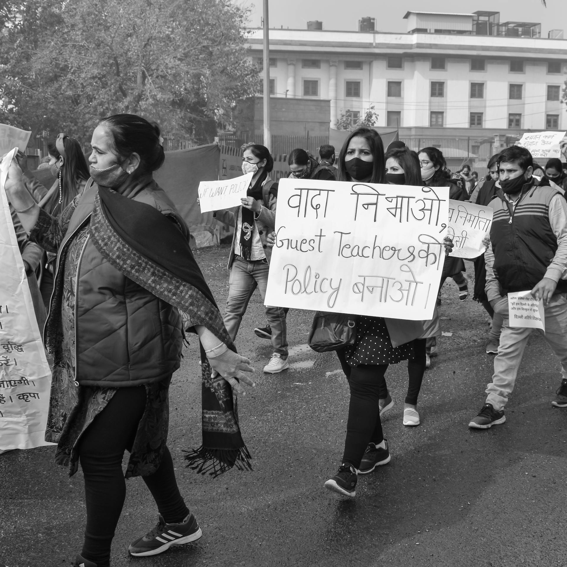 Black and white photo of a street protest for guest teacher policy reform, featuring diverse participants.