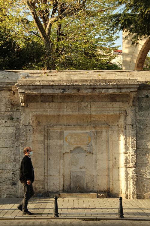 Free A man in a face mask walks past a historical stone wall in İstanbul, Türkiye. Stock Photo