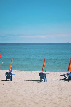 Vibrant beach scene with chairs and umbrellas by the ocean under a clear blue sky.