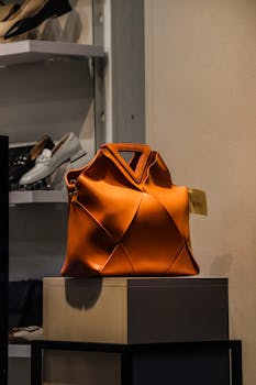 A striking orange designer handbag showcased elegantly on a stand in a retail store.
