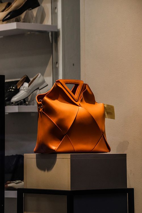 Free A striking orange designer handbag showcased elegantly on a stand in a retail store. Stock Photo