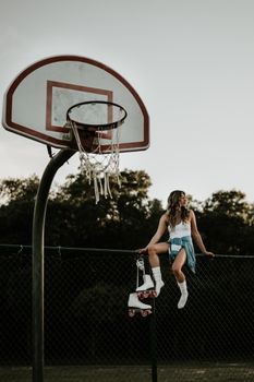 A woman with roller skates sits on a fence near a basketball court, exuding a retro vibe.
