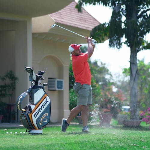 Free Man in Orange Shirt and Gray Shorts Playing Golf Stock Photo