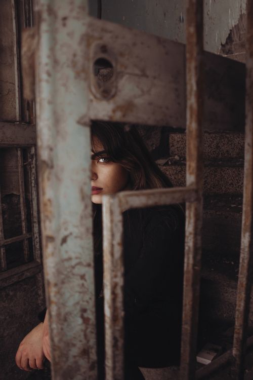 Free A mysterious and artistic portrait of a woman partially obscured by rusty metal bars in a dim setting. Stock Photo