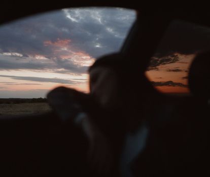 Blurry view of a peaceful traveler resting in a car with a dramatic sunset sky in the background.
