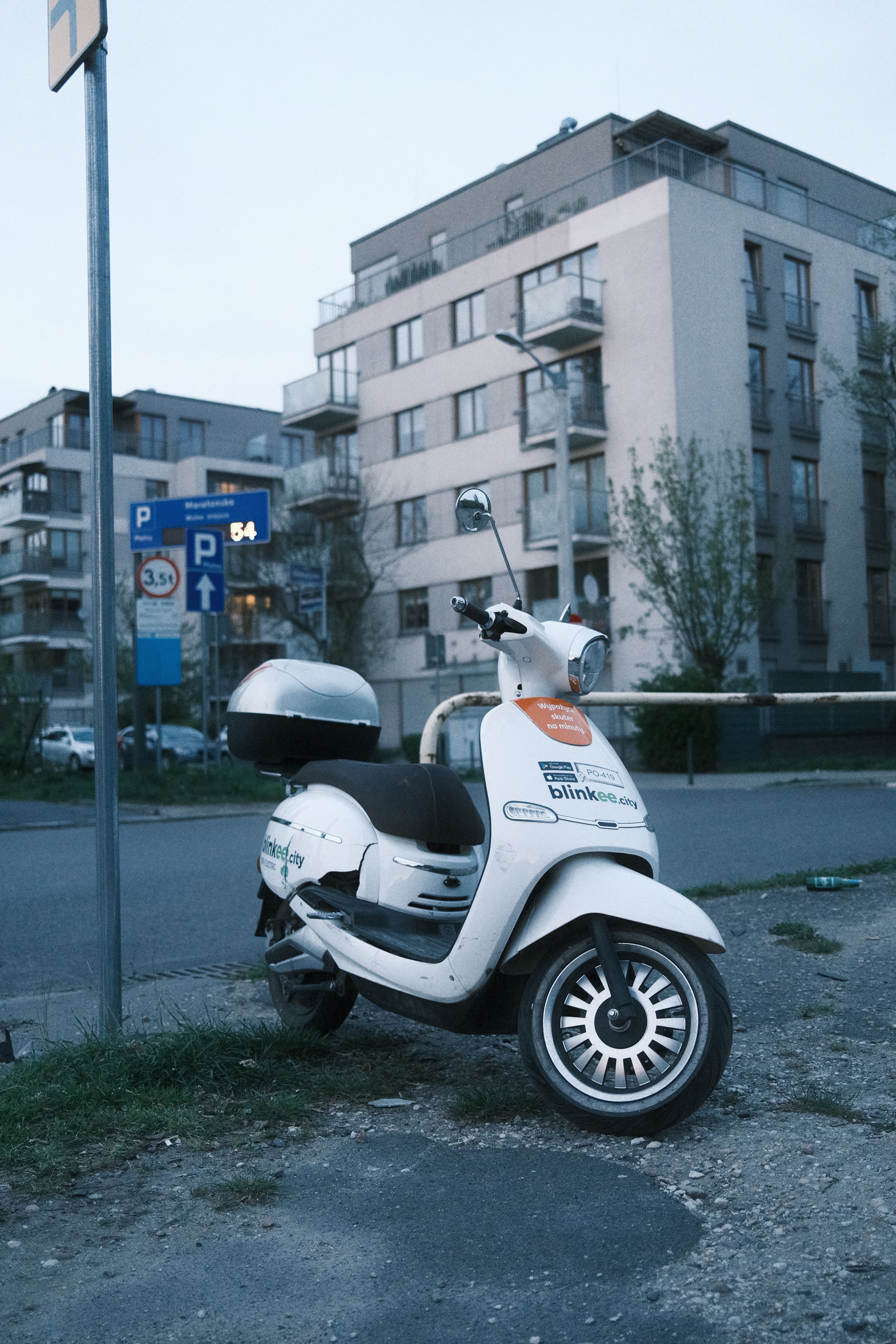 A white scooter is parked beside modern apartment buildings in Poznań, Poland, creating a serene urban street scene.