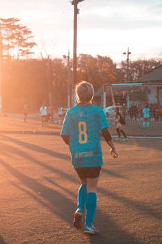 日落时分，青少年女孩们在足球场上身着球衣，展示运动技能与团队合作