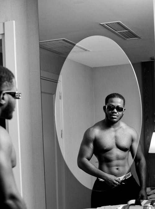 Free Topless Man Wearing Sunglasses Looking at His Own Reflection on the Mirror Stock Photo