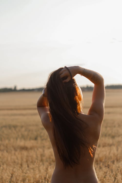 Back View Shot of a Topless Woman Standing on a Brown Field