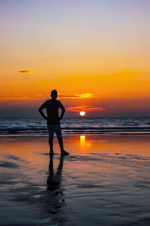 Free A person stands in silhouette at sunset on a tranquil beach, reflecting leisure and peace. Stock Photo