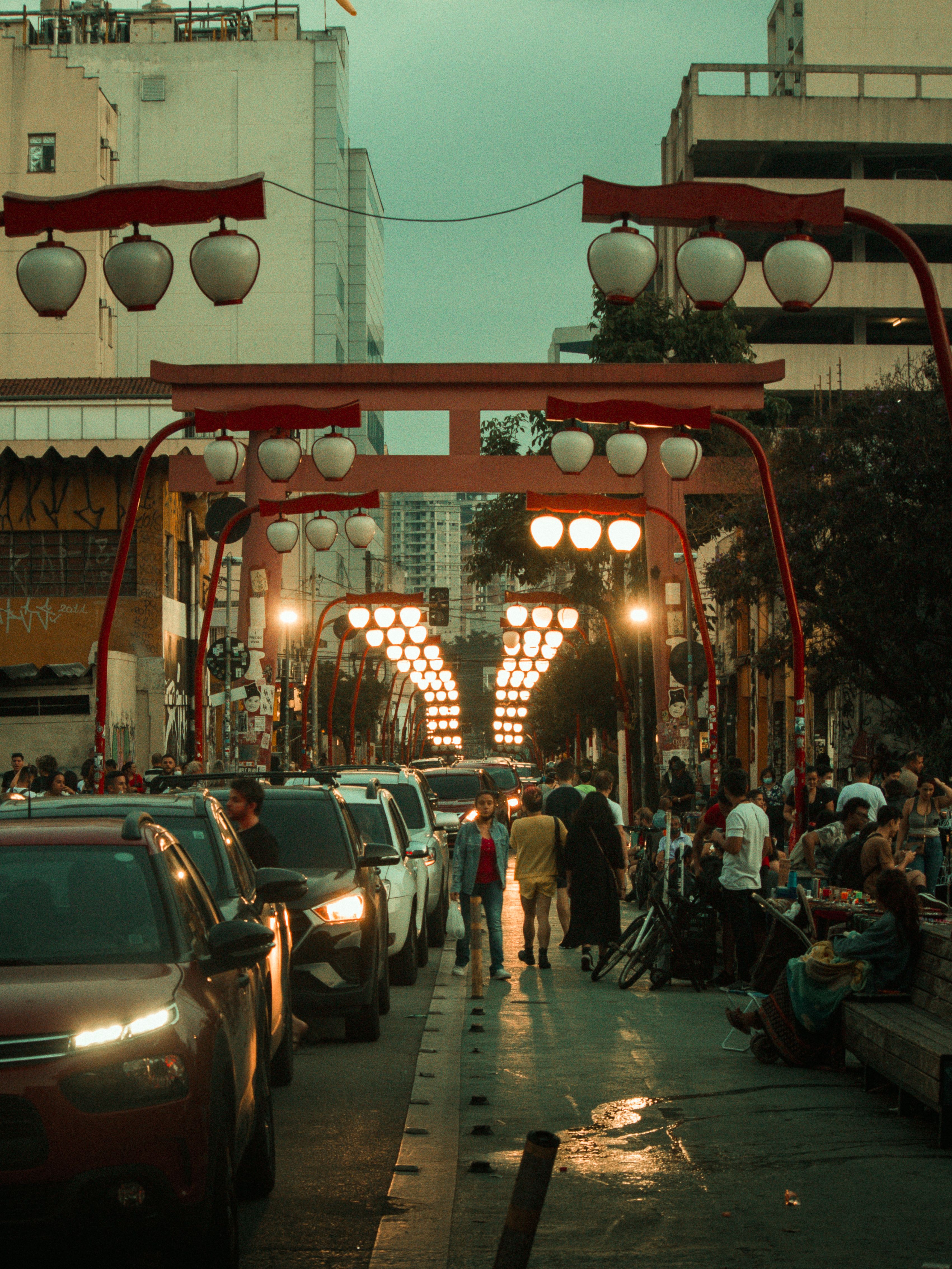 A bustling street with Asian lanterns and traffic during dusk, capturing urban life.