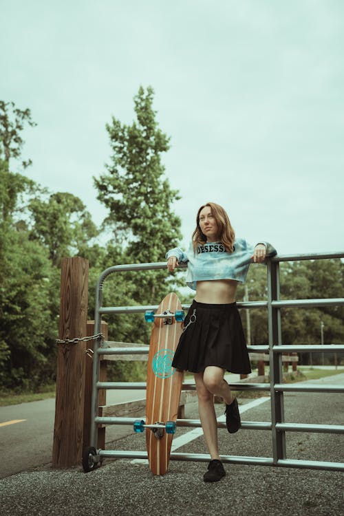 Woman in Crop Top and Black Skirt Standing on Metal Fence 